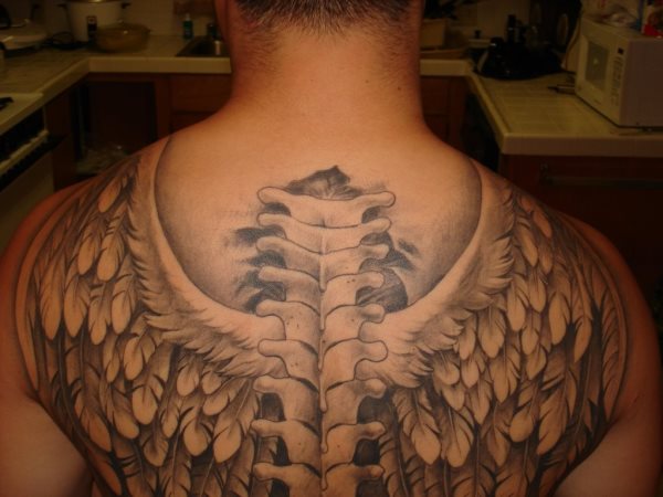 Tatuaje de una columna vertebral en la espalda de la que le salen unas enormes alas de ave de color blanco y que se han acompañado con otras plumas que hacen las veces de alas y recorren toda la espalda