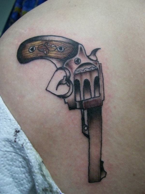 Tatuaje de un revolver con la culata de madera y que para darle un toque original se ha diseñado la forma de un corazón en el gatillo, esperemos que este tatuaje tan amoroso, dispare flores y amor