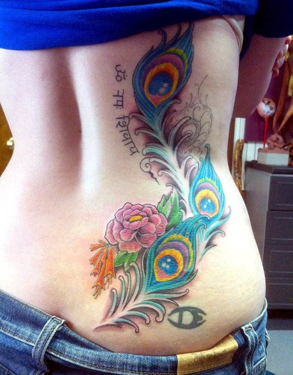 Tatuaje femenino compuesto por unas cuantas de plumas de pavo real en el costado, realizada avarios colores y que parece estar inacabado, tatuaje al que se le ha completado con una pequeña palabra o frase al rededor del plumaje