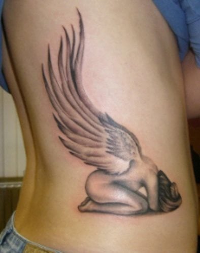 Tatuaje de una mujer ángel que se encuentra desnuda y agazapada sobre el suelo, con dos grandes alas