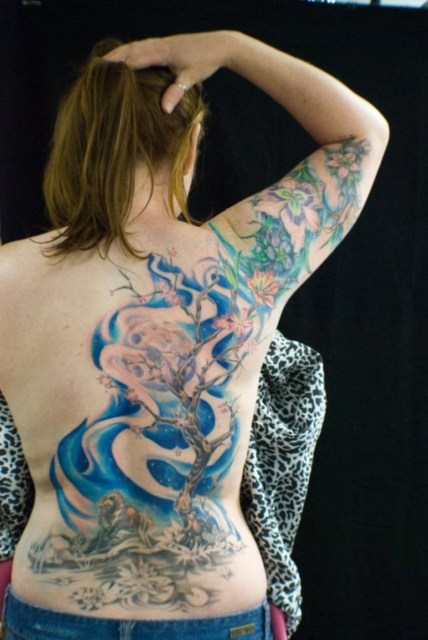 Precioso tatuaje en la espalda que recorre con un cielo azul que le sienta genial y llega hasta el brazo donde tiene tatuado unas flores, el tatuaje es súper bonito, tanto por su dibujo, forma, pero sobre todo, por los colores seleccionados y el predominio del color azul
