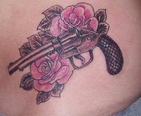 Tatuaje de una pistola del tipo revolver sobre dos rosas acompañadas de unas hojas que envuelven a todo el tatuaje