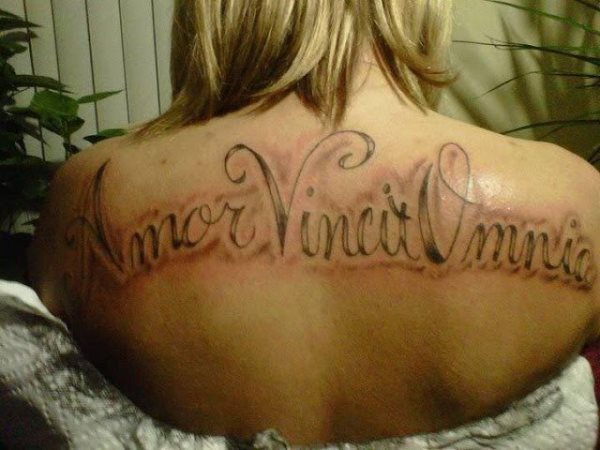 Tatuaje en la espalda con letras capitales de gran tamaño en el que dice Amor Vincit Omnia, un gran tatuaje con una frase sencilal y directa, en el que tal vez sobra el sombreado que va rodeando a la frase