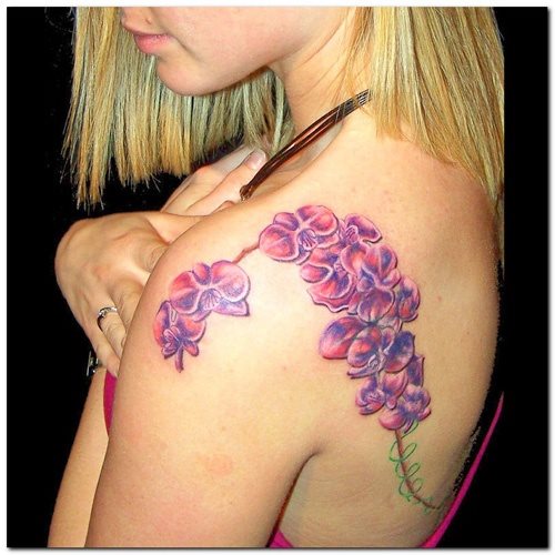 Tatuaje de ramilletes de flores que recorre desde el hombro hasta bajar por la espalda y donde los colores que se han utilizad son el azul y el rojo en tonos pasteles, un tatuaje que por su forma y recorrido, nos gusta mucho