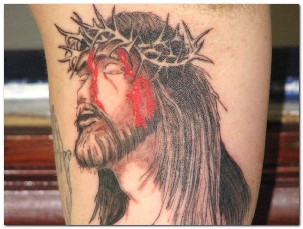 Tatuaje de Cristo crucificado con gran pelo y barbas, además de la características corona de espinas, en esta ocasión los restos de sangre característicos por tener clavada la corona de espinas, no se han conseguido demasiado bien y se ha abusado del color rojo de la sangre