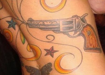 Diseño de tatuaje de una pistola para el que se han tatuado unas líneas de colores, estrellas y mariposas que salen del cañón de la pistola