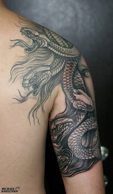 Tattoo sobre el hombro y parte del brazo con varias serpientes y se ve de fondo el rostro de una mujer