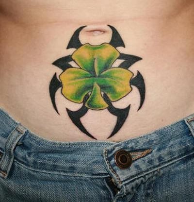 Trébol y tribales conjugan una mezcla atrevida para este tatuaje bajo el ombligo, en el que se ha hecho un buen uso de los colores, el verde para el trébol y el negro para el tribal, pero en el que destacan las buenas sombras conseguidas para este trébol de la buena suerte