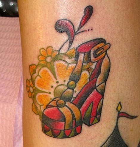 Este tatuaje nos gusta mucho por varios motivos, entre ellos porque es un gran complemento a otros tatuajes y también nos gusta los colores que se han utilizado para tan peculiar zapato, el cual nos hemos tenido que detener un rato para areciarlo bien, al igual que la flor amarilla y verde que completa al zapato de mujer