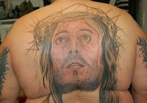 Tatuaje en la espalda de un gran semblante de la cara de Jesucristo mirnado hacia el cielo, como se puede apreciar el tatuaje aún no está terminado o eso nos parece y se ha rellenado con un suave color rojizo toda la cara