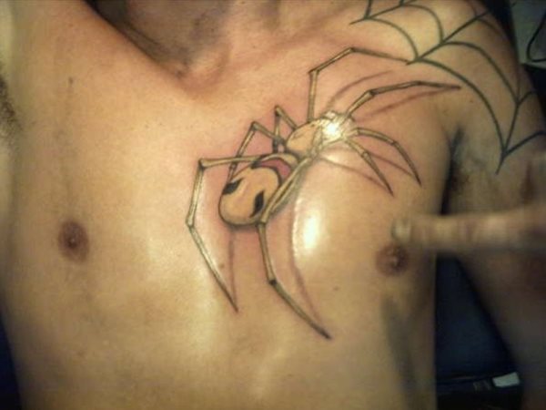 Esta araa de cuerpo amarillento se acerca hacia el tatuaje de una tela de araa que cubre todo el hombro