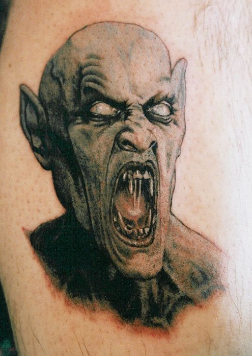 Tatuaje de un vampiro que da mucho miedo, por las grandes orejas de pico que se lan realiado, la mirada de enfado con los ojos blancos y unos grandes colmillos tanto en la parte superior como inferior de la mandíbula