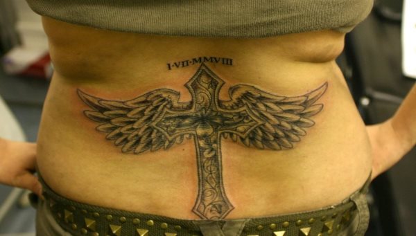 Tatuaje en la cintura de una cruz alada, en el que en la parte superior de la cruz se ha tatuado una fecha en números romanos, la verdad es que es un tatuaje sencillo en cuanto a elementos: una cruz, alas y una fecha, pero que se han cuidado mucho los pequeños detalles, como se puede apreciar en el interior de la cruz