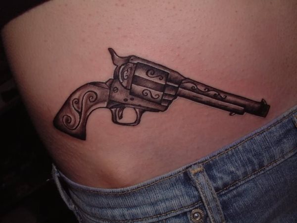 Tatuaje de un revolver a color negro sobre el abdomen, para el que se han tatuado algunas líneas sobre la pistola