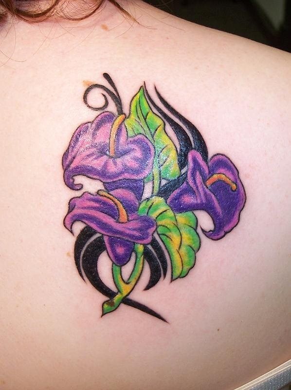 Tatuaje en el pecho de unas flores moradas con unas grandes hojas verdes y unos ramilletes emulando algunos trazos tribales, un tatuaje muy femenino y en una zona muy elegante, que se lucirá con facilidad