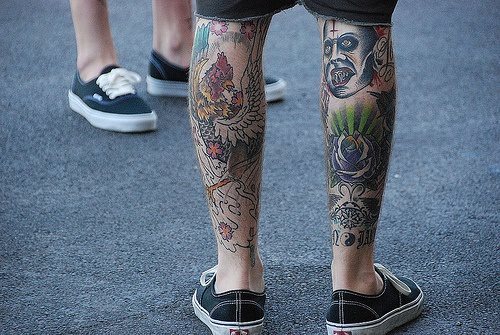 Tatuaje en los gemelos con varios diseños  y colores diferentes, es un tipo de tatuaje muy típico de los skaters, como es la indumentaria que podemos observar en este chico, al que algunos tatuajes le quedan por rellenar