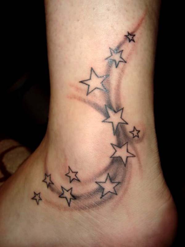 Tatuaje de un conjunto de pequeñas estrellas sobre un sombreado muy difuminado que va bajando por la pierna, rodeando el tobillo, hasta llegar al pie, un tatuaje que ha quedado precioso y que creemos alcanzaría la perfección si se rellenan de color las estrellas