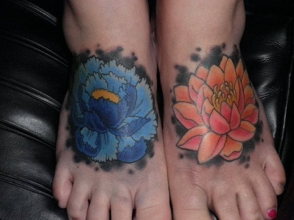 Tatuaje en el empeine, en esta ocasión se pueden apreciar sendas flores en cada empeine del pie, el tatuaje del empeine del pie izquierdo es una flor naranja de pétalos acabados en punta y la flor del tatuaje del empeine del pie derecho es una flor de colores celestes y azules