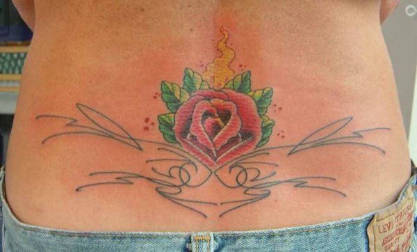 Tatuaje en el centro de la cintura de una rosa roja, rodeada por unas hojas verdes y un pequeño humo amarillo, además se le han añadido unas cenefas excesivamente finas, sin acabados demasiado espectaculares