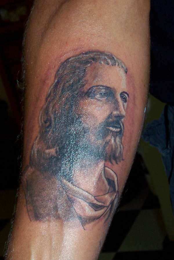 Tatuaje del semblante de Jesucristo, tatuado sobre el brazo y con una gran profundida de la mirada, tal vez el detalle que más destaque de todo el tatuaje, por que ni el pelo largo ni las barbas han sido tatuados con gran nitidez