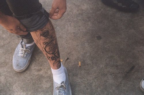 Tatuaje en la pierna izquierda de varios dibujos, que ocupan gran parte de la piel y que no han sido rellenados, ni coloreados