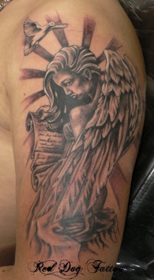 Tatuaje de un ángel con un papiro en las manos y del que resaltamos la gran belleza de este ángel y los destellos de luz que parecen sobresalir de su propio cuerpo, además se le ha añadido una preciosa paloma en pleno vuelo cerca de la cabeza del ángel, un resultado espectacular el de todo el tatuaje