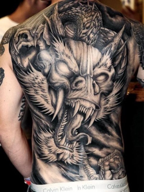 Tatuaje en toda la espalda, que no deja ni una parte de la piel sin tatuar, en el que se puede apreciar la cabeza de un dragón con enormes colmillos, parte del cuerpo y las garras abiertas a punto de cazar