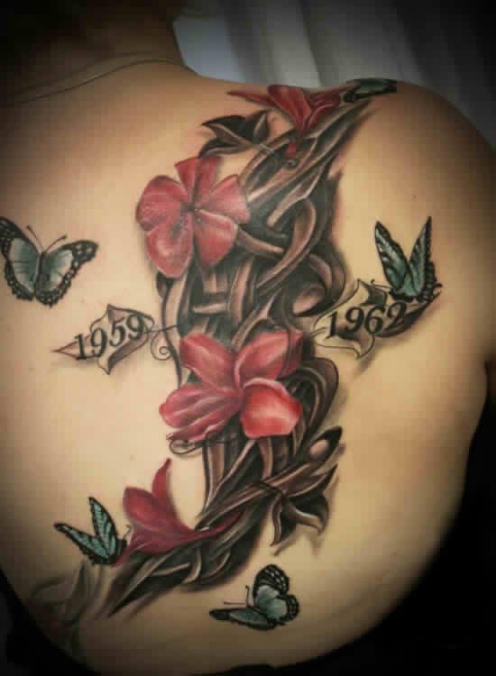 Tatuaje en hombro y espalda de una enredadera de flores a la que acompañan algunas mariposas volando alrededor, como se puede observar en una de las hojas se ha tatuado la fecha 1959 y en la otra hoja la fecha 1962