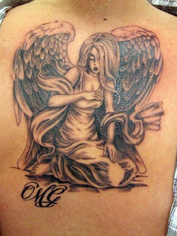 Tattoo de una mujer ángel de rodillas con un ceñido vestido de gran escote envuelta con una especie de fular y a la que se ha caracterizado con un pelio largo que cubre gran parte de su rostro y le da un aspecto aún más misterioso y sensual