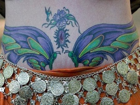 Precioso tatuaje de dos libélulas en colores azul y verde, donde podemos observar que en el ombligo se ha tatuado un sol con una flor lila arriba