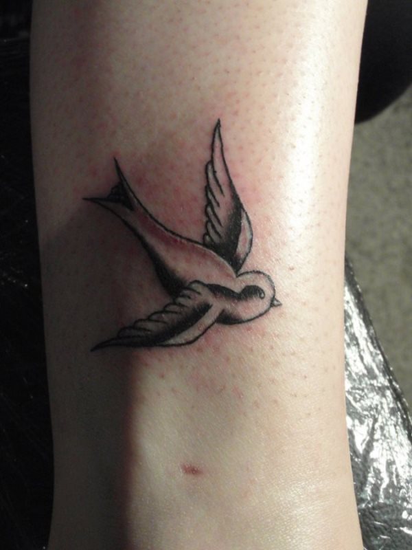 Tatuaje de una sencilla golondrina sobre la pierna, estamos ante un tatuaje de trazos finos y poco detalles, cuya grandeza reside precisamente en no adornar el ave con elementos innecesarios y dejar el color negro para que haga las veces de silueta y sombreados