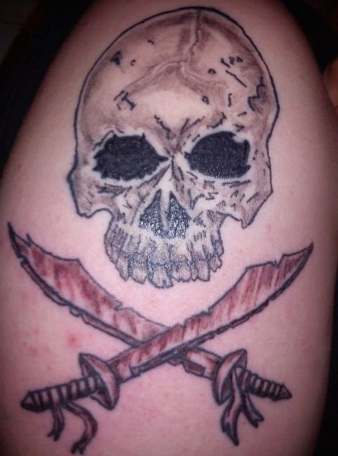 Tatuaje pirata de una calavera cuyos huesos inferiores típicos de las calaveras han sido sustuidos por dos espadas piratas cruzadas, estamos ante el clásico amante del mundo pirata y el mundo marinero, un tatuaje que podría haber tenido una mejor elaboración