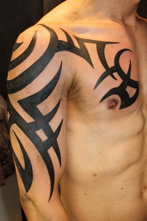 Brazo y pecho tatuado con un enorme tribal de color negro que se verá bien ya desde lejos y que seguro se han tenido que utilizar bastantes horas para confeccionar este tatttoo, ya que como vemos, los trazos son bastante largos y gruesos y han tenido que ser rellenados a color negro