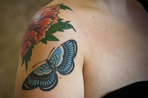 Original diseo de una mariposa llena de detalles que acude a una flor situada en el hombro