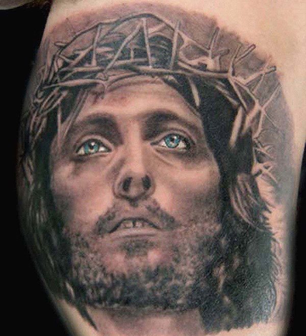 Tatuaje del rostro de Jesucristo con la corona de espinas y al que se le ha añadido la peculiaridad de tintar los ojos de color celeste, un bonito detalle para resaltar de un tatuaje que precisamente no es característico por su originalidad