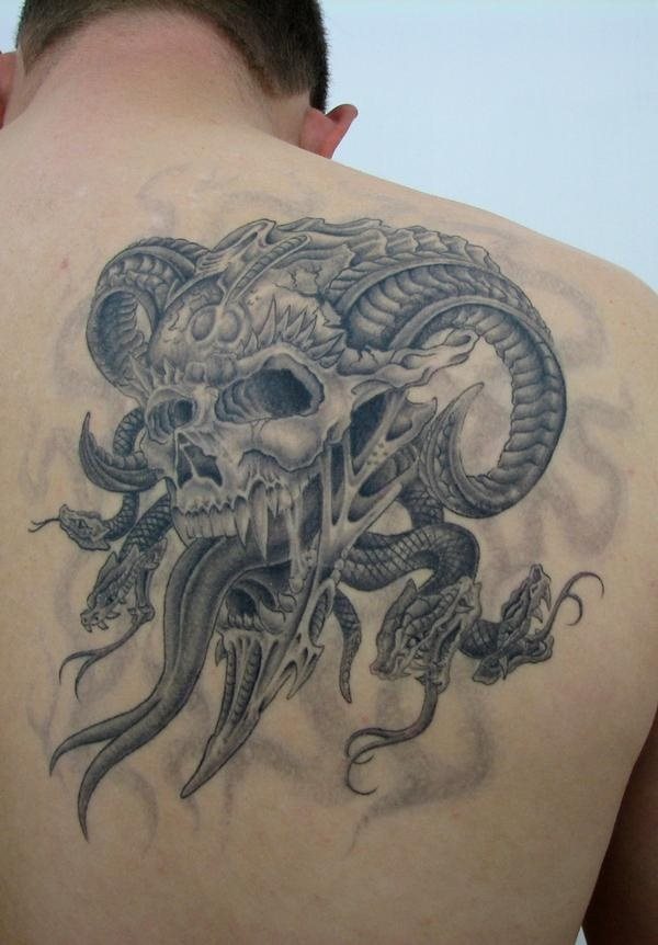 Tatuaje sobre la espalda de una calavera con cuernos que tiene un gran tamaño y para la que sólo se ha utilizado el color negro y una gran cantidad de sombreados