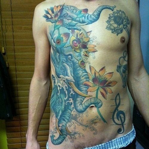 Tatuaje precioso de dos elefantes azules sobre el pecho y abdomen, acompañados de unas flores también preciosas y que han dado un resultado genial, al que ha ayudado la gran cantidad de arrugas sombreadas sobre el tattoo, que le dan ese aspecto de matrícula de honor