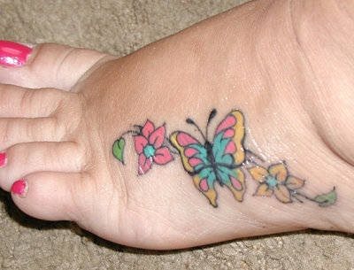 Colorida mariposa rodeada de florecillas en tonos dulces, que destaca por ser un tatuaje pequeño, coqueto y disimulado que transmite una gran alegría y que tiene la suerte de ser un tatuaje que con cualquier zapato cerraro no se vería y así podríamos enseñar sólo cuando nos apeteciera que se viera