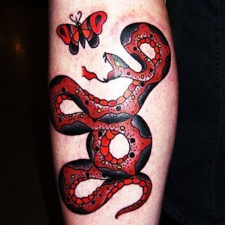 Tatuaje de una serpiente roja y negra que parece estar a punto de comerse una mariposa, también del mismo color, de este tattoo nos gusta como se ha conseguido un gran resultado combinando solamente des colores y nos gusta mucho como el rojo de la parte inferior de la serpiente destaca muchísmo sobre el resto de la serpiente de un rojo más tostado