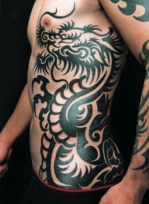 Tatuaje de un dragón tribal sobre el pecho, costado y abdomen, tatuado a color negro y utilizando trazos gruesos donde predominan la grna cantidad de acabados en punta, un tatuaje que no se ve a menudo y que ha quedado genial pintado sobre el cuerpo de este hombre
