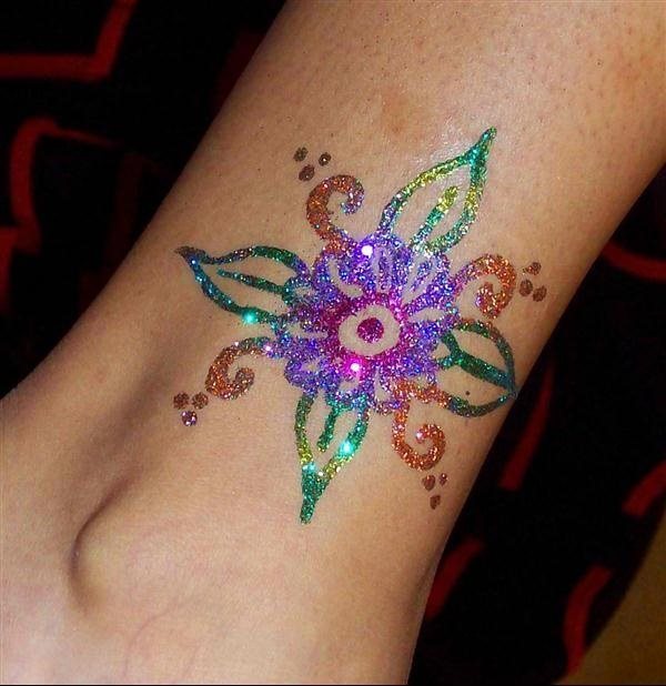 Tatuaje de una flor colorida que parece haber sido realizado con algún tipo de pinturas o brillantinas, se ve claramente que es un tatuaej que se borra con agua, pero que estamos convencidos a que si se decidiera a hacerse alguno parecido en esa zona, le quedaría genial