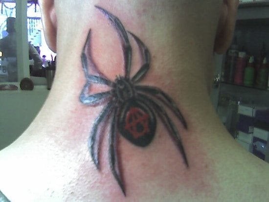 Tattoo en la nuca de una araña de gran tamaño en cuyo cuerpo se ha tatuado en rojo la A de anarquía