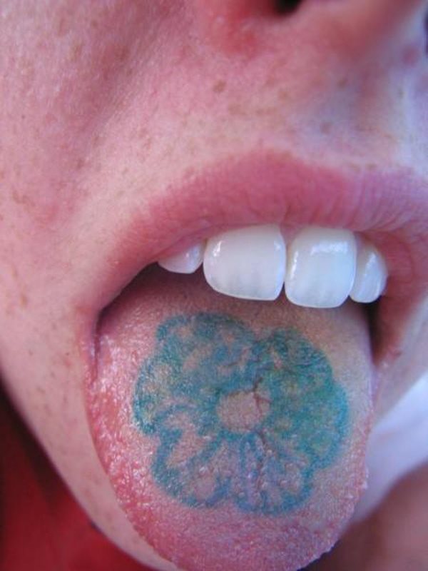 Tattoo de una flor en la lengua, es una especie de flor con pétalos pequeños y en tonos azules, que esta chica ha decidido tatuar en su lengua, suponemos que para asegurarse de que nadie tendrá un tatuaje parecido, ya que una flor es muy probable que se repita, pero encontrarla tatuada en la lengua, ya será más difícil