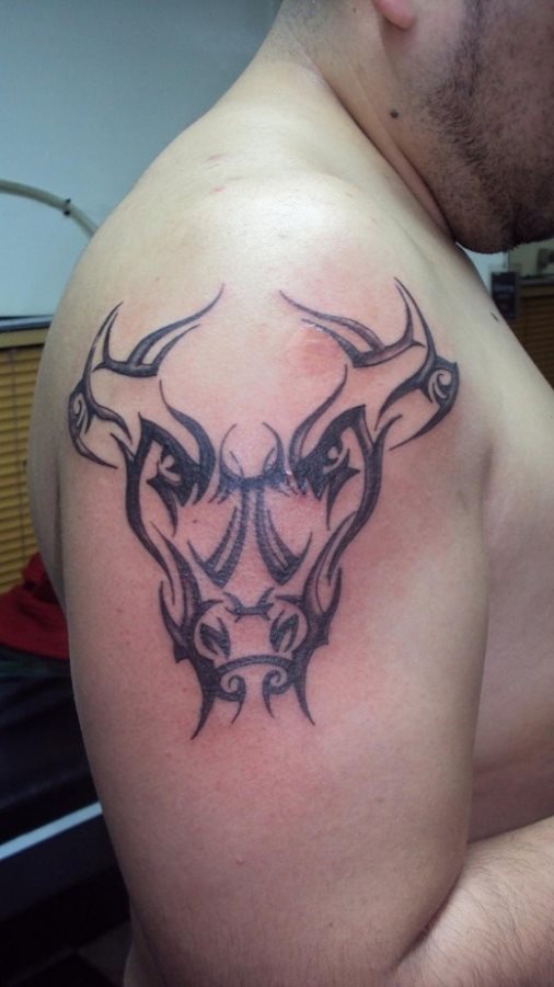 Tatuaje en el brazo de unos signos tribales que van compomiendo la silueta de lo que parece un animal, nos aventuraremos y diremos que es un toro y que tal vez represente al segundo signo del Zodiaco, es decir, a Taurus, es un signo de naturaleza negativa y de cualidad fija, representado por un toro con astas circulando a su alrededor