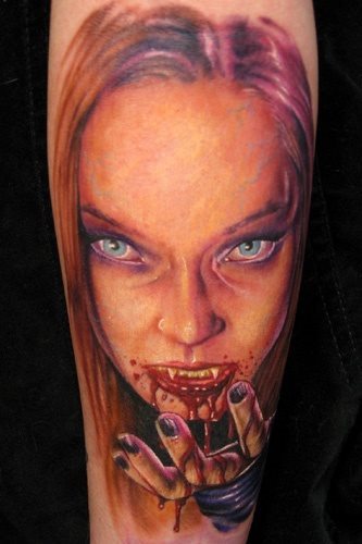 Tatuaje de una mujer vampiro con la boca llena de sangre y a la que se le ha dibujado una prominente frente, siendo sinceros, este tattoo nos gusta bastante y creemos que es por lo bien conseguida que está la cara y lo bien insertada que está con los propios colores de la piel de esta persona