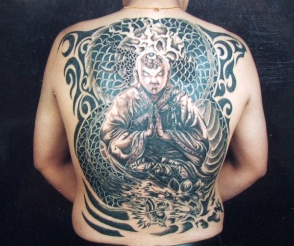 Tatuaje de lo que parece un budha rodeador por un gran fondo de escamado de dragón en el que en la cintura se aprecia la cabeza y que ha sido completado con unos tribales que van rodenado todo el tattoo