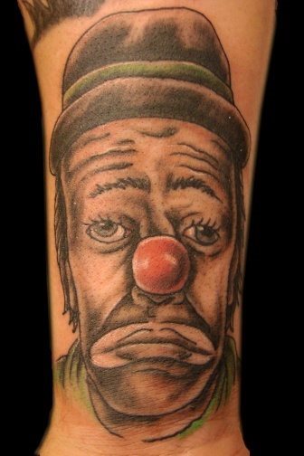 Diseño de tatuaje de un payaso triste con un sombrero que le da un toque muy de los años sesenta, las cejas y la mirada perdida le dan ese toque de tristeza que parece quiere transmitir este tatuaje, en qel que las líneas no destacan demasiado gracias al buen hacer del tatuador a la hora de trazar las sombras