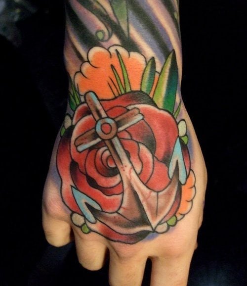 Diseño de un ancla y flor en la mano, con un gran colorido que parecen dar punto y final a todo un tatuaje que baja por el brazo, el ancla con una cruz parece tener un doble significado y la flor que hay denajo tiene unos pétalos muy bien rematados gracias al color rojo y el sombreado en tonos negros, por cierto, gran acierto el de incluir algunos remates en color naranja