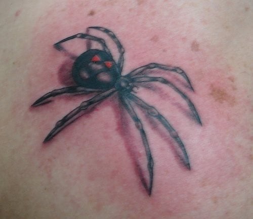 Tatuaje de una araña negra con dos triángulos rojos, de la que nos gustaría destacar lo bien que ha quedado la cabeza de la araña y como se pueden apreciar toods los pequeños detalles de este insecto, un buen trabajo
