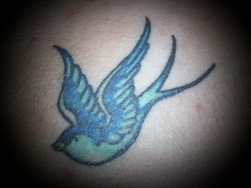 Tatuaje de una golondrina en tonos azules y turquesas, cuyo pico se ha pintado de color amarillo, estamos ante uno más de los miles de tattoos de golondrinas que en esta galería que aquí os presentamos podréis ver